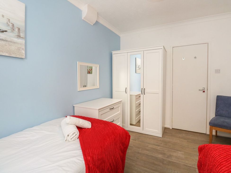 A bedroom with a single bed with red blanket and towels a white wardrobe and dresser a blue chair and a door at Old Malthouse Apartment in Weymouth