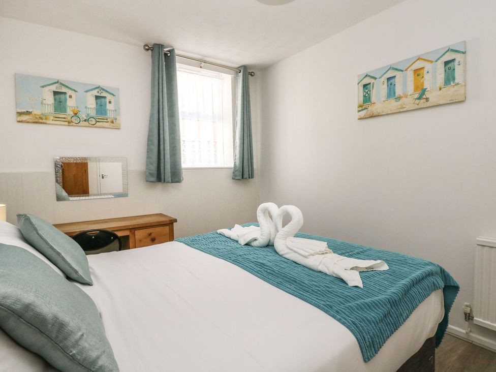 A bedroom with a bed covered with teal bedding and towels folded in swan shapes at Old Malthouse Apartment in Weymouth