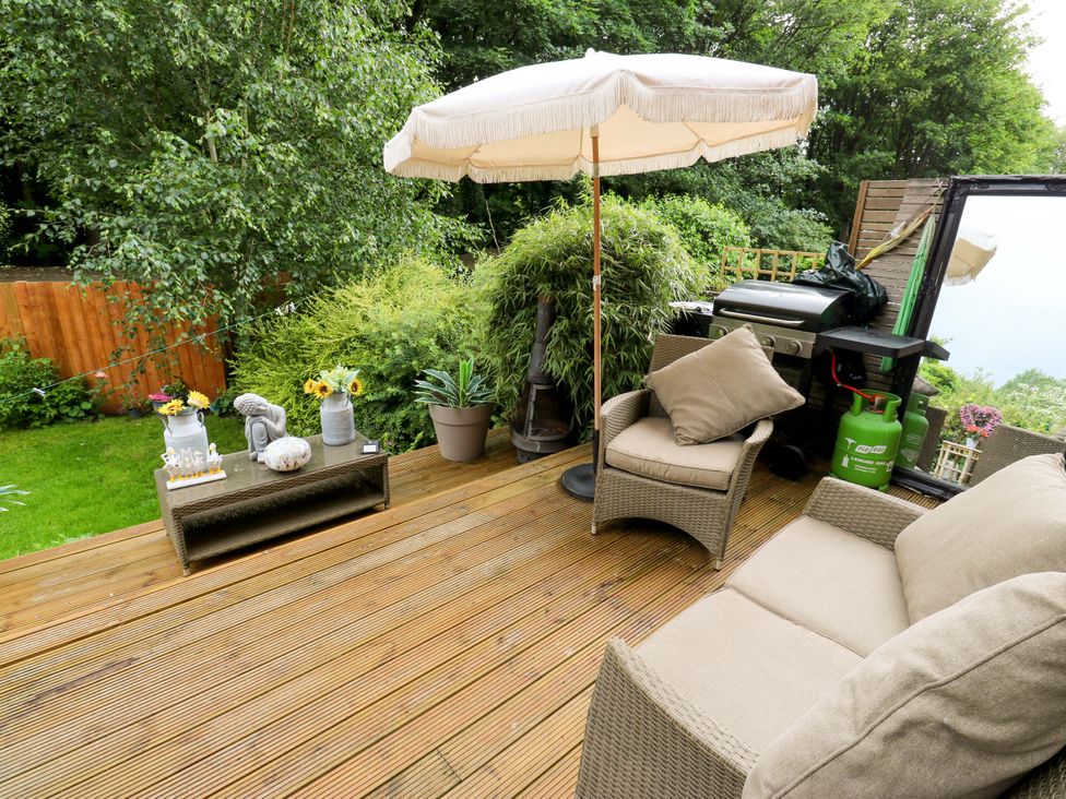 A garden with a wooden deck, chairs, table, and barbecue at St Mary's House in Oldham