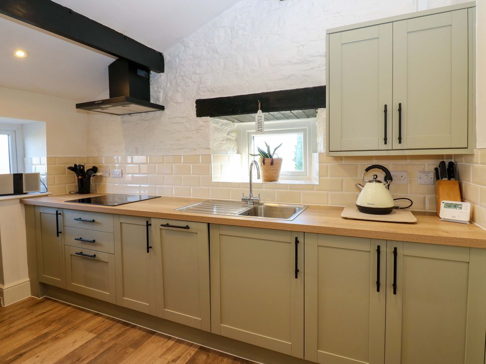 A kitchen with cabinets, sink, kettle, and window at Eastend Cottage