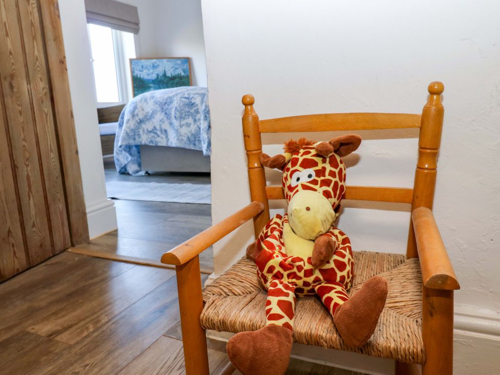 A stuffed giraffe on a chair with a bed and picture in the background at Eastend Cottage