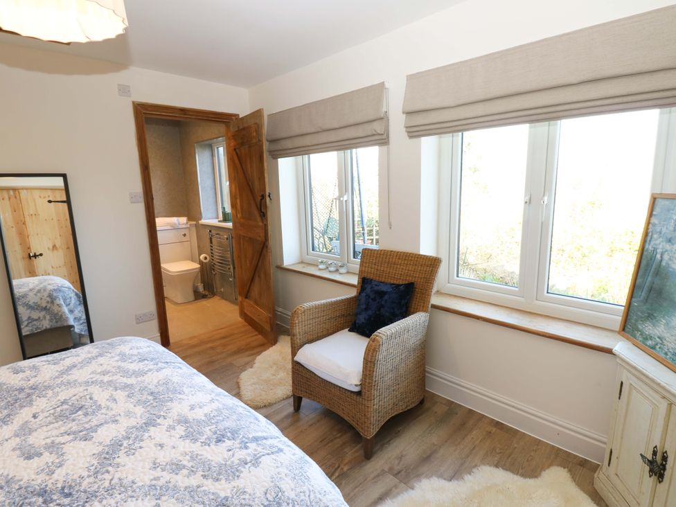 A bedroom with a chair and windows at Eastend Cottage