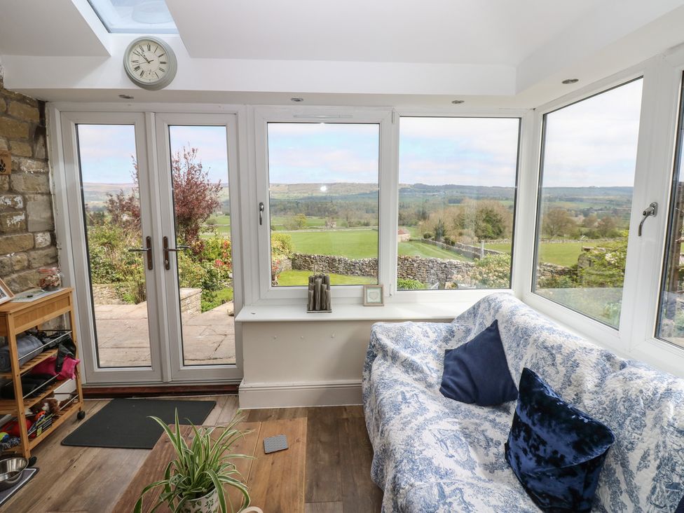 A conservatory with a sofa and views of the garden at Eastend Cottage in West Witton