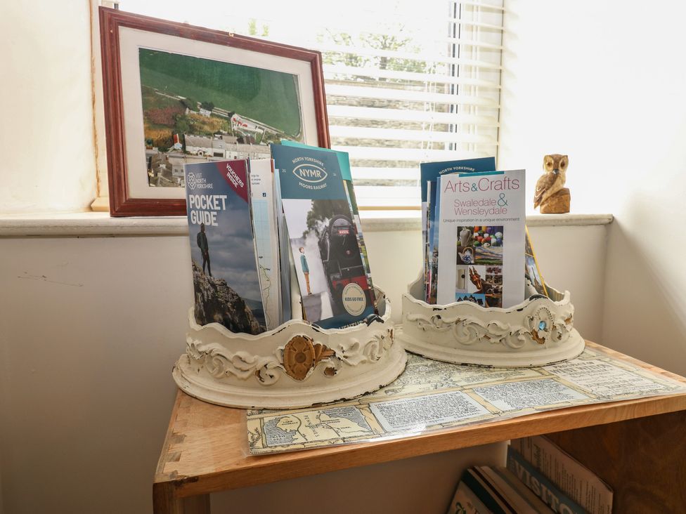 A table with brochure holders and a framed picture at Eastend Cottage in West Witton
