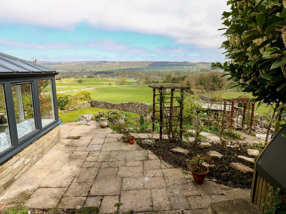 A garden view with a conservatory and patio at Eastend Cottage in West Witton