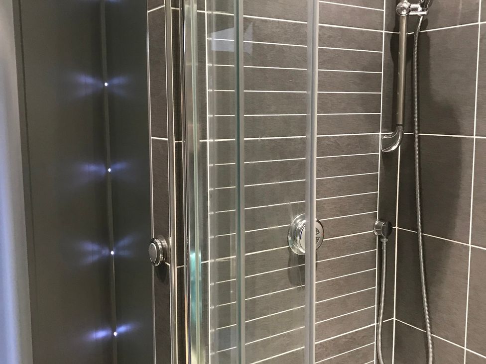 A shower enclosure with glass panels and a shower head at Sea Views No 8 Plas Darien in Trearddur Bay