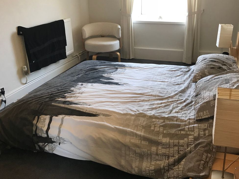 A bedroom with a bed, chair, and curtains at Sea Views No 8 Plas Darien Trearddur Bay