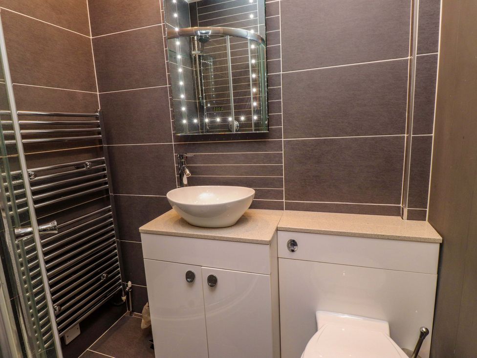 A bathroom with a shower, toilet, sink, mirror, and towel radiator at Sea Views No 8 Plas Darien in Trearddur Bay