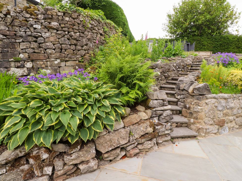 A garden with stone walls, steps, and various plants at Rose Tree Cottage in Skipton