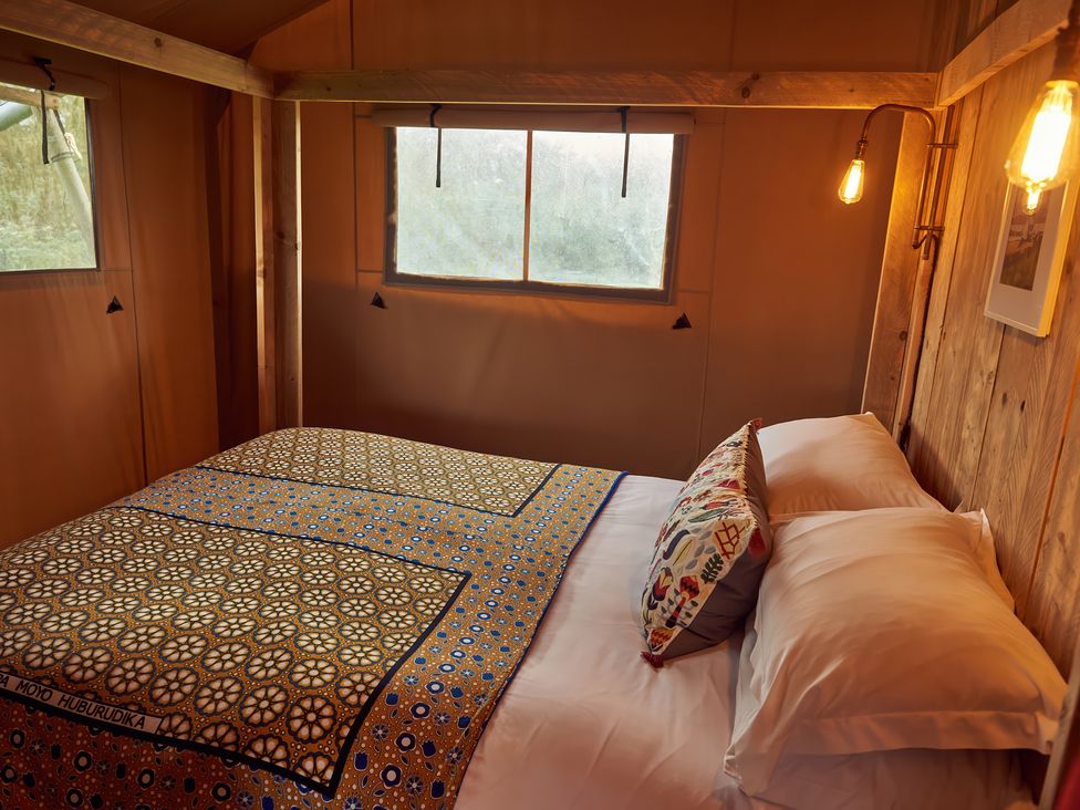 A bedroom with a double bed covered with patterned blankets and pillows inside a wooden cabin