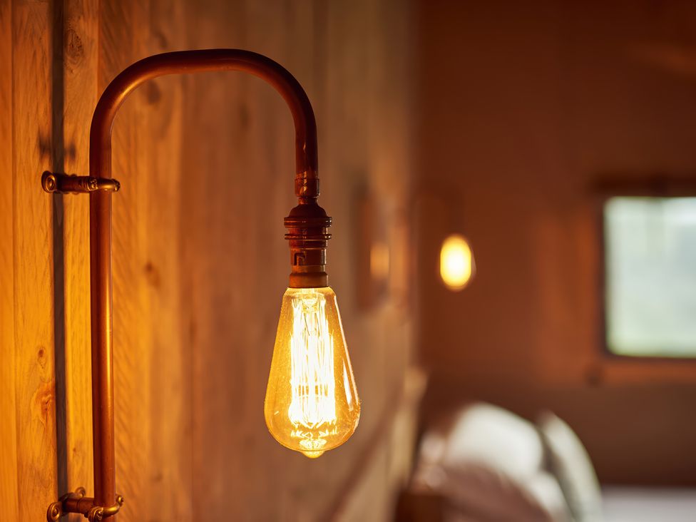 A close up of a lit vintage light bulb on a wall fixture in a wooden room at Bramley Lodge in Coxbridge near Glastonbury