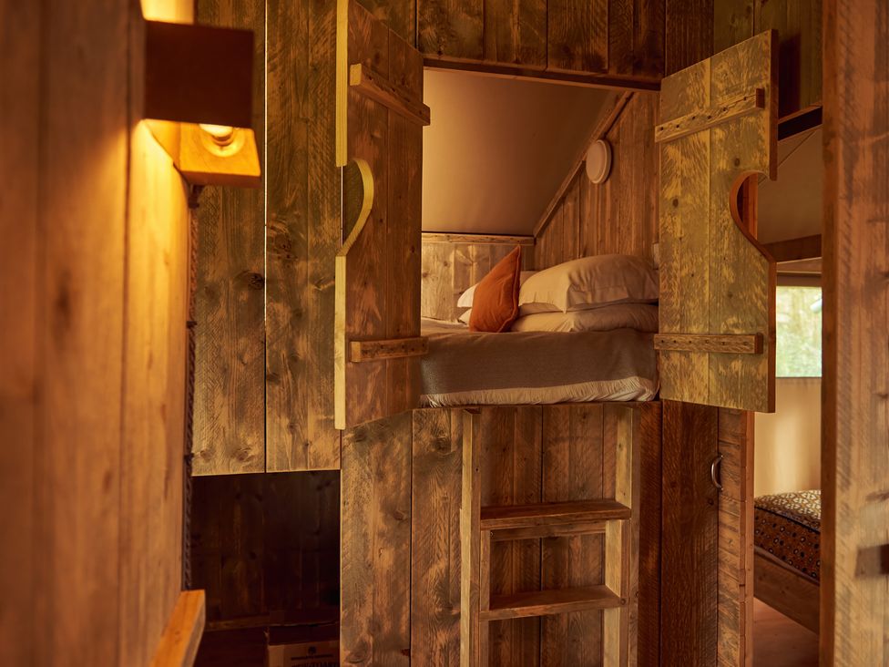 A wooden room with a small loft bed accessed by a ladder and a bedroom visible through a doorway at Bramley Lodge in Coxbridge near Glastonbury