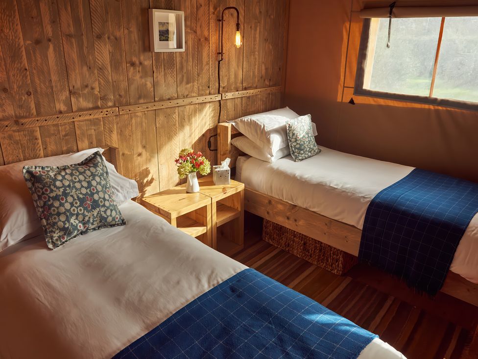 A bedroom with two single beds with blue throws and patterned pillows separated by a wooden nightstand with flowers at Bramley Lodge Coxbridge near Glastonbury