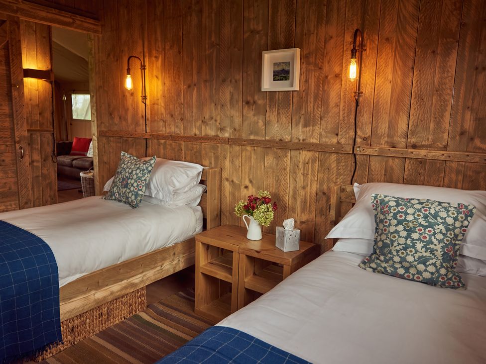 A bedroom with two single beds wooden walls and a small wooden table with flowers at Bramley Lodge Coxbridge near Glastonbury