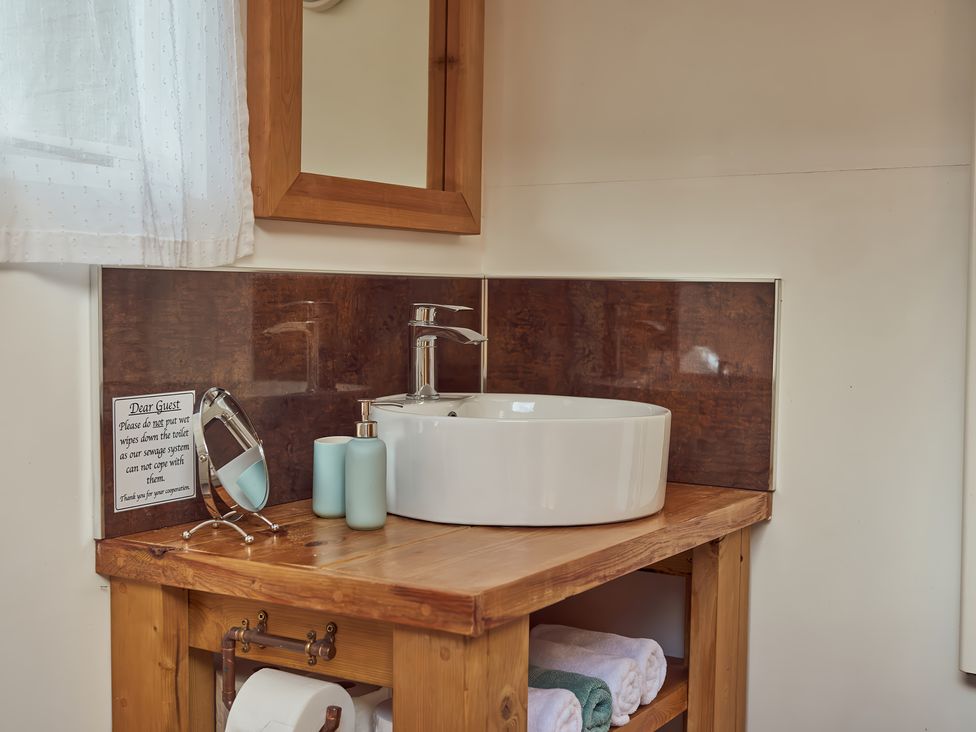 A bathroom sink with a round white basin on a wooden countertop with a mirror soap dispenser and towels at Bramley Lodge in Coxbridge near Glastonbury