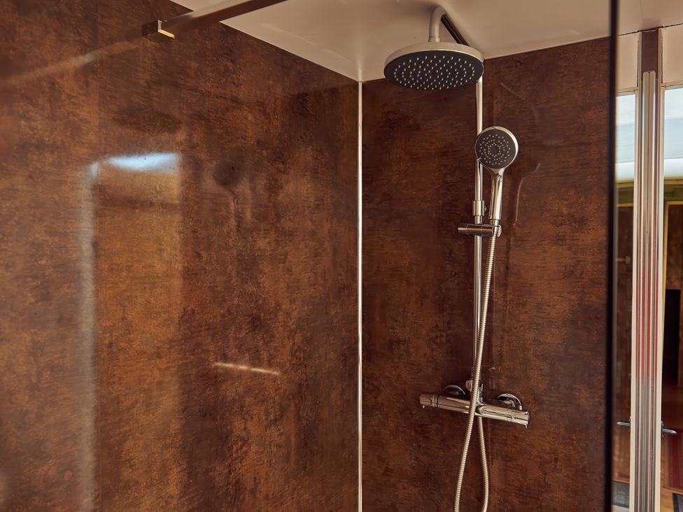 A shower with a dual showerhead fixture in a bathroom with brown textured wall panels at Bramley Lodge in Coxbridge near Glastonbury