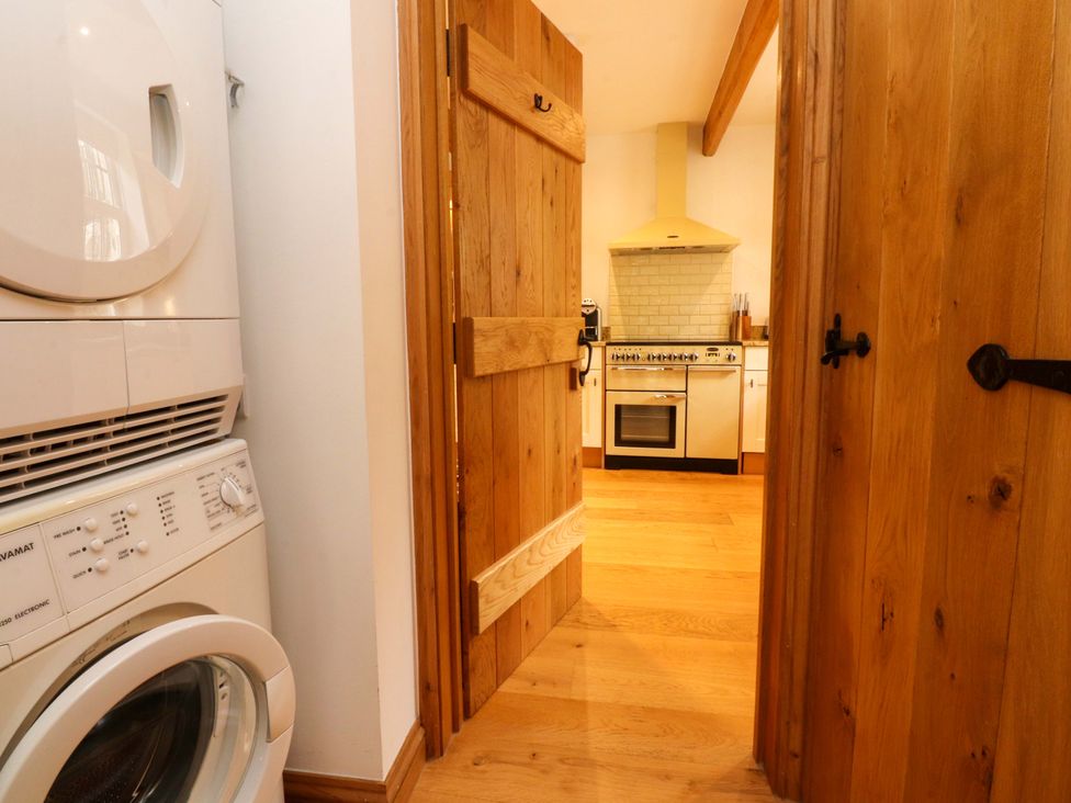 A laundry room with a washing machine and dryer leading to a kitchen at Rowan Tree Cottage in Skipsea