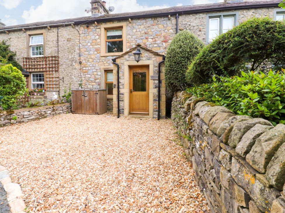 A stone wall and gravel driveway with a wooden door at Welly Bob Cottage in Airton