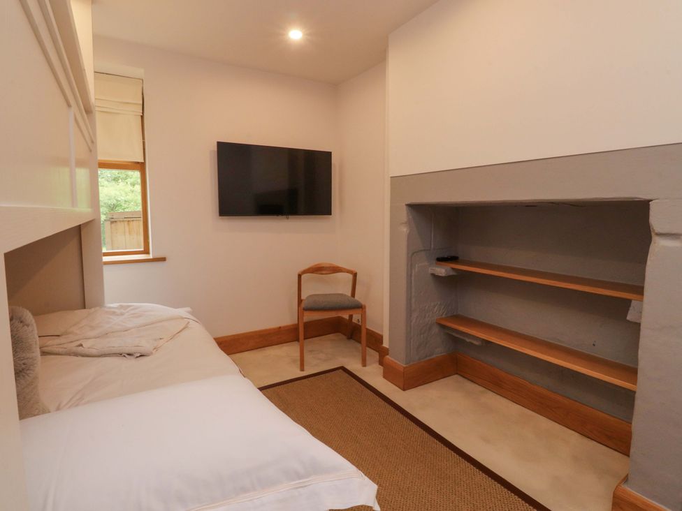 A bedroom with a bed, chair, television and shelf at Welly Bob Cottage in Airton