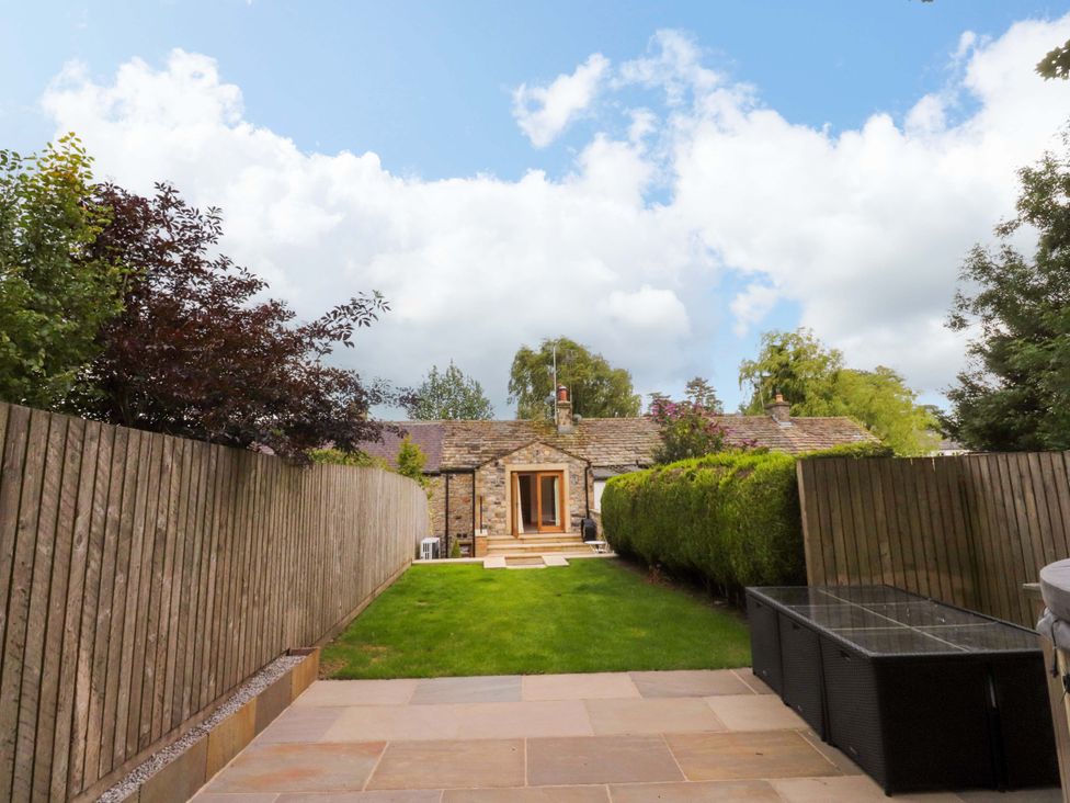 A garden with grass and a stone patio at Welly Bob Cottage in Airton