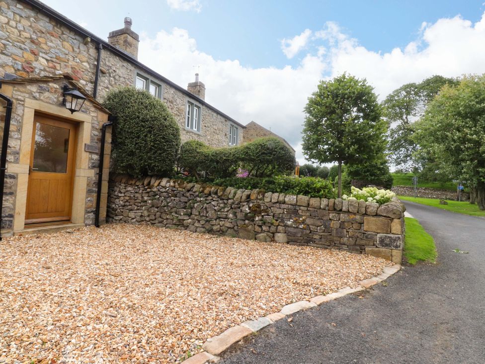A stone house with a wooden door and gravel entrance at Welly Bob Cottage in Airton