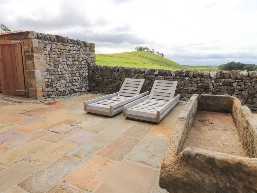 An outdoor patio with sun loungers and a stone wall at Carden Laithe Barn in Threshfield