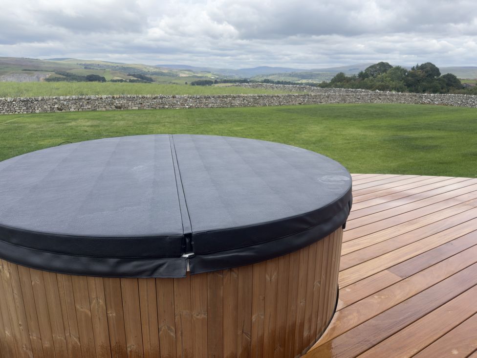 A hot tub on a wooden deck with a landscape view at Carden Laithe Barn in Cracoe