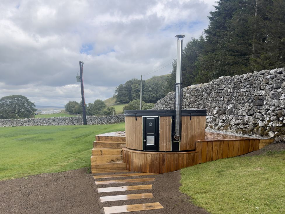 A hot tub on a wooden deck surrounded by grass and a stone wall at Carden Laithe Barn Cracoe