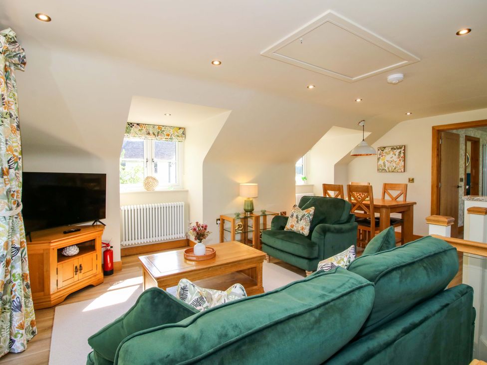 A living room with a sofa, television, and dining area at The Hideaway in Longden
