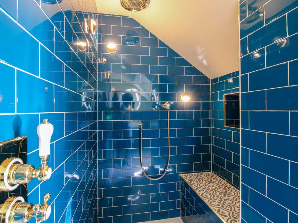A bathroom with blue tiled walls and a shower setup at The Hideaway in Longden