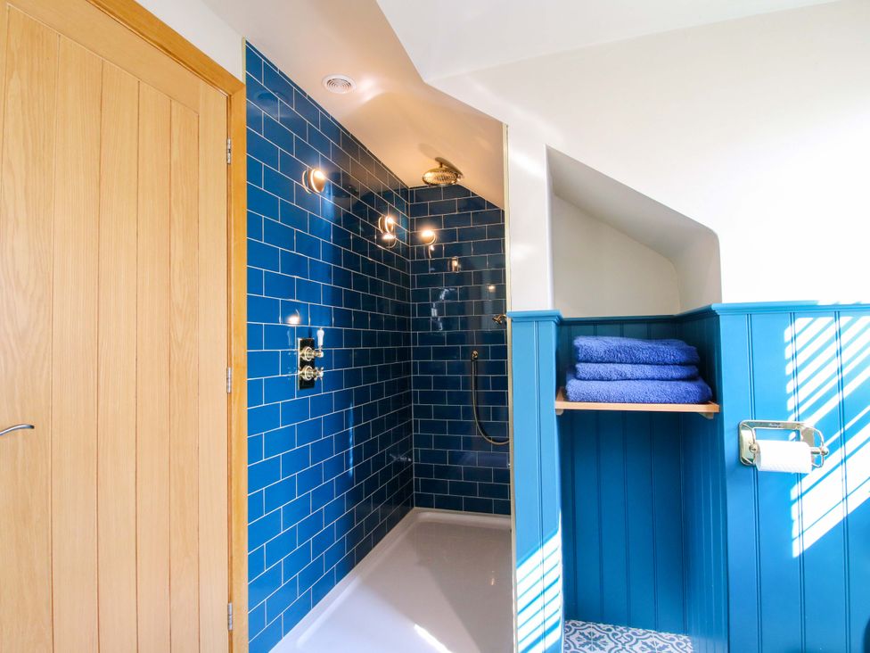 A bathroom with a shower and towels on a shelf at The Hideaway in Longden