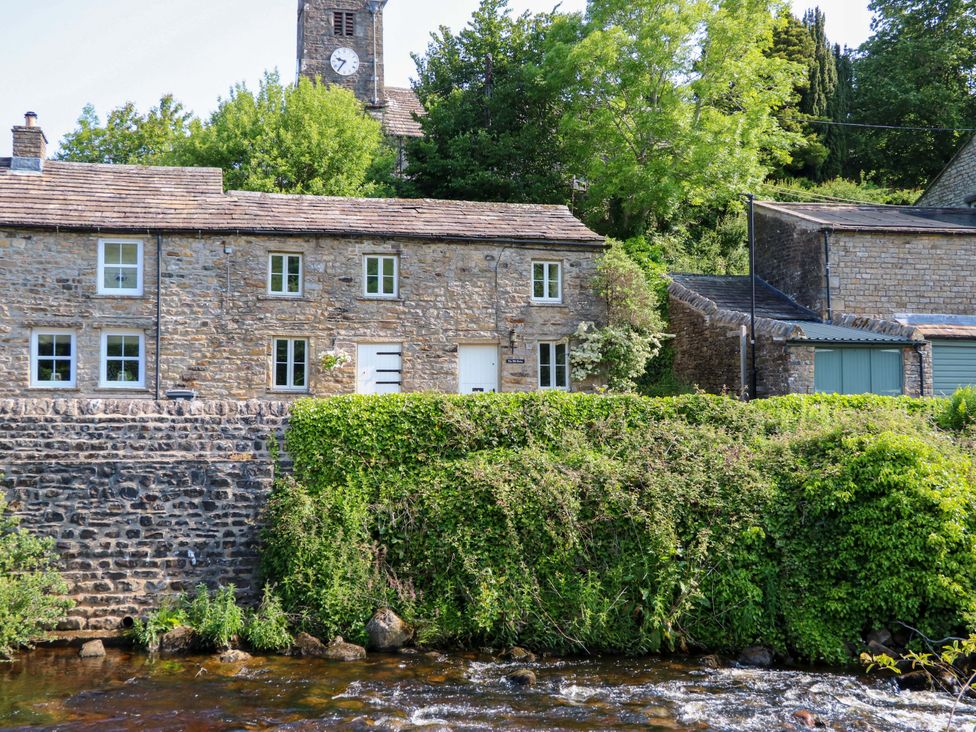 A stone house near a river with trees and a clock tower at The Old Dairy in Richmond