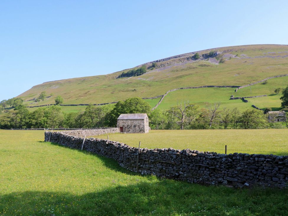 A stone barn in a grass field with a dry stone wall and trees at The Old Dairy in Richmond