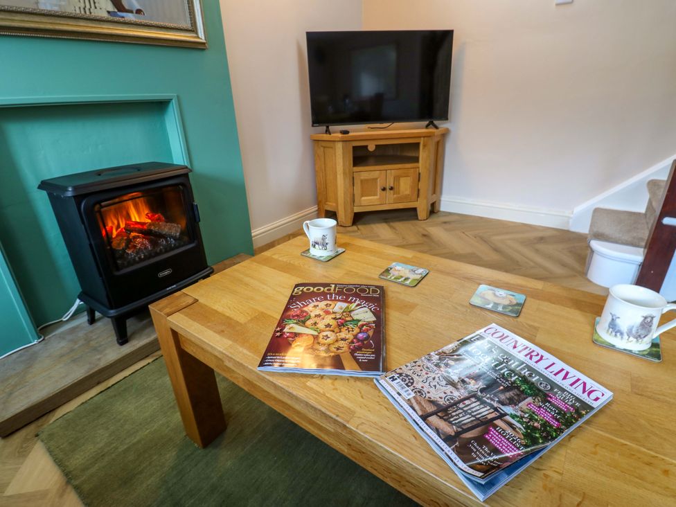 A living room with a stove, television, coffee table, and magazines at The Old Dairy in Muker