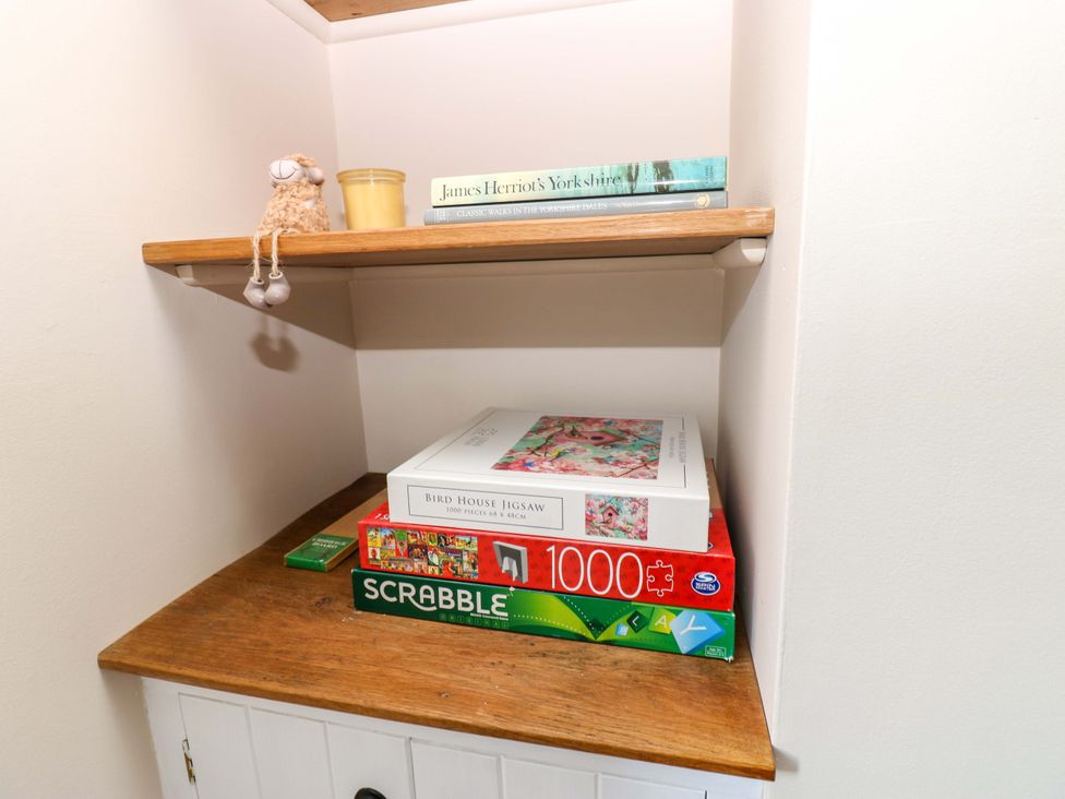 A shelf with books, a jigsaw puzzle, a board game, and a figurine at The Old Dairy in Muker