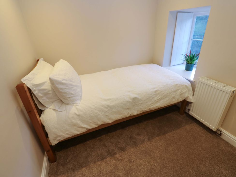 A bedroom with a single bed and a window with a plant at The Old Dairy in Muker