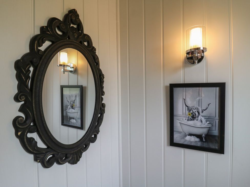 A decorative oval mirror reflecting a framed picture of a dog in a bathtub on a white paneled wall at The Heron in Lode near Bottisham