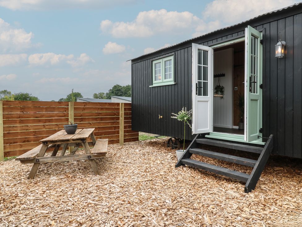 An outdoor area with a wooden picnic table and a small building with open double doors at The Heron in Lode near Bottisham