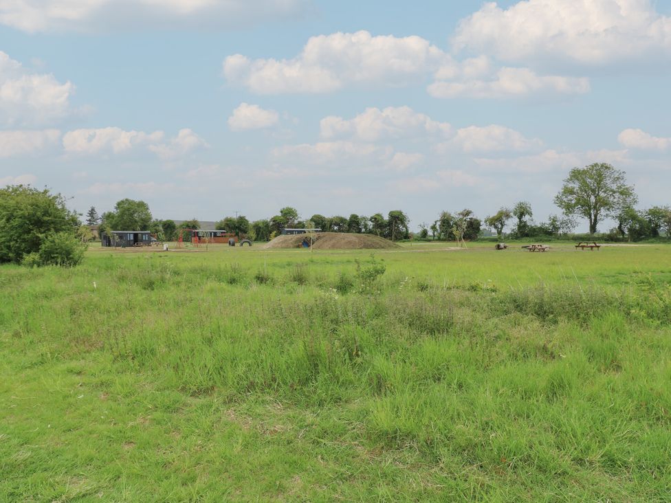 A grassy open field with playground equipment and picnic tables under a cloudy sky at The Heron in Lode near Bottisham