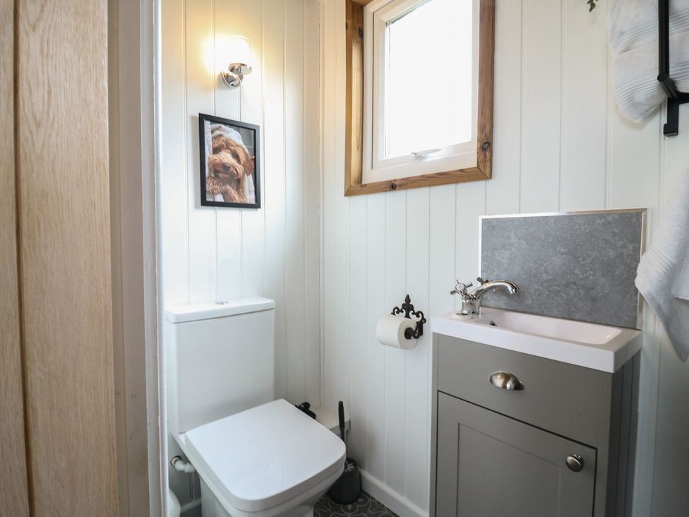 A small bathroom with a toilet sink window and a framed picture of a dog above the toilet at Barn Owl in Lode near Bottisham