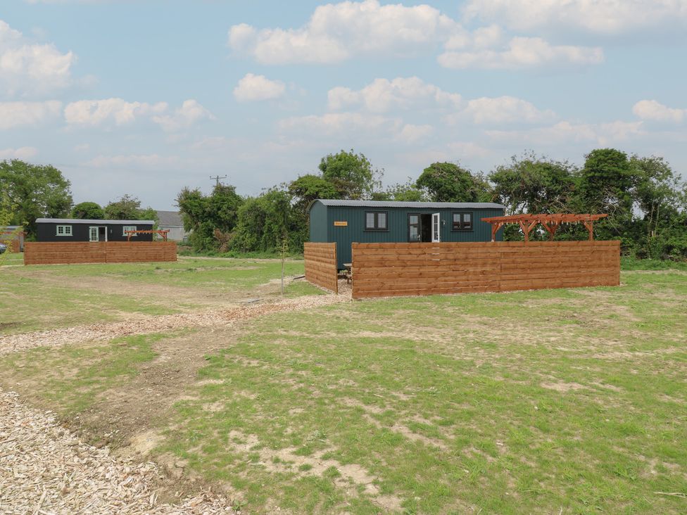 Two small buildings with fenced yards on a grassy field with a dirt path and trees in the background at Barn Owl in Lode near Bottisham