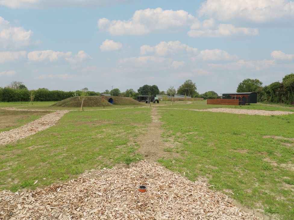 An open grassy field with wood chip paths a mound with a blue tunnel and some structures in the background at Barn Owl in Lode near Bottisham