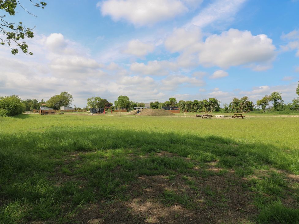 A grassy field with picnic benches and play equipment in the distance at Barn Owl in Lode near Bottisham