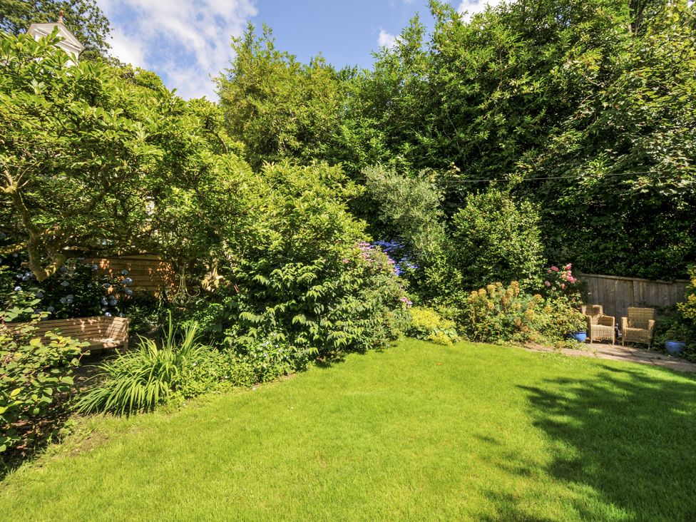 A garden with grass, flowers, a bench, and chairs at Trenare in Truro