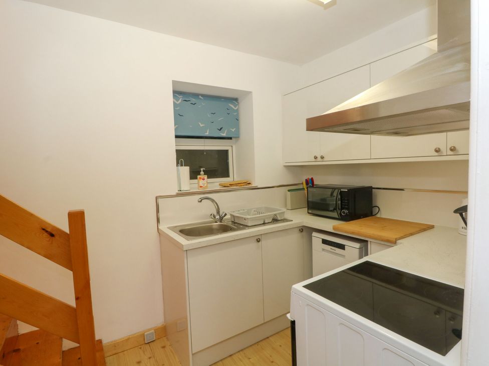 A kitchen featuring sink, microwave, stove, and wooden stairs at Holme Cottage in Hebden Bridge