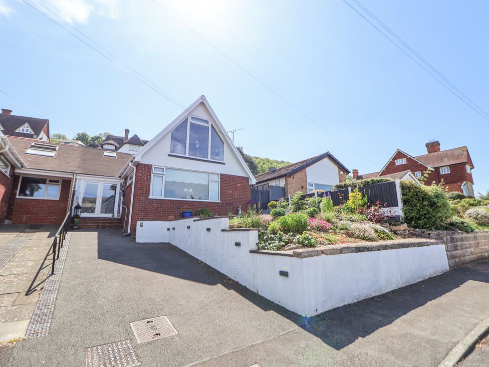 A brick house with a large window and sloped roof next to a garden and driveway at 67 Pendre Avenue in Prestatyn