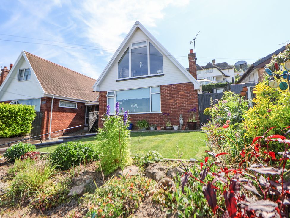 A brick house with white upper facade and large windows with a front garden at 67 Pendre Avenue in Prestatyn