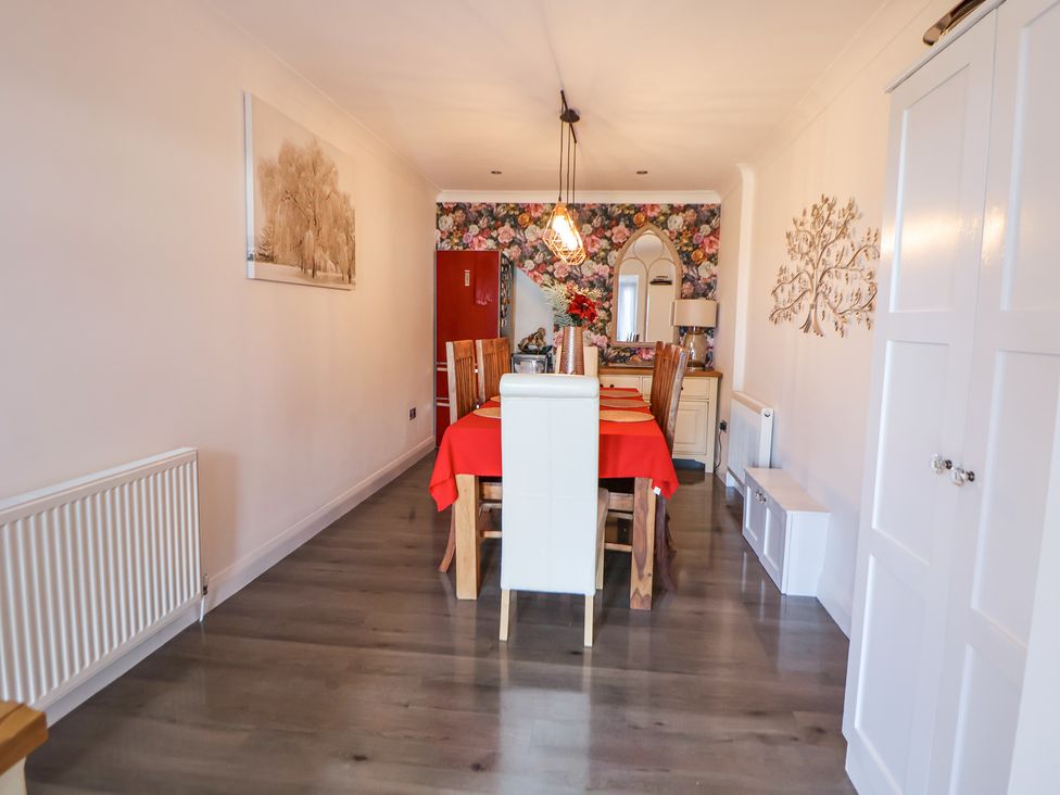 A dining room with a wooden dining table covered with a red tablecloth and wooden chairs in front of a floral wallpapered wall at 67 Pendre Avenue in Prestatyn