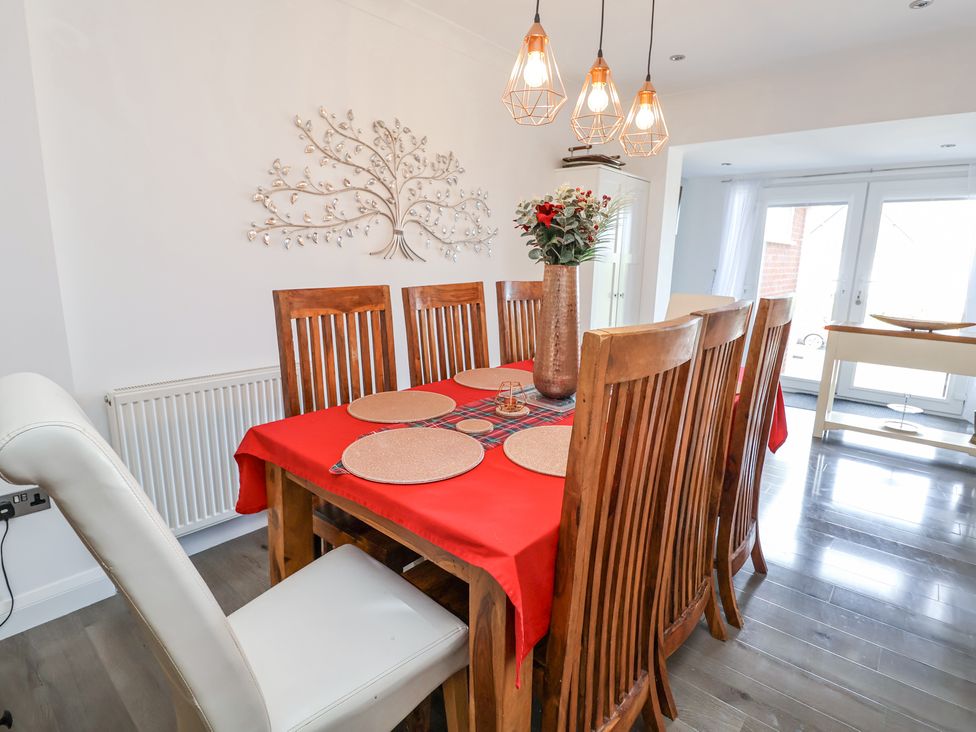 A dining room with a wooden table and chairs a red tablecloth and a vase with flowers at 67 Pendre Avenue in Prestatyn
