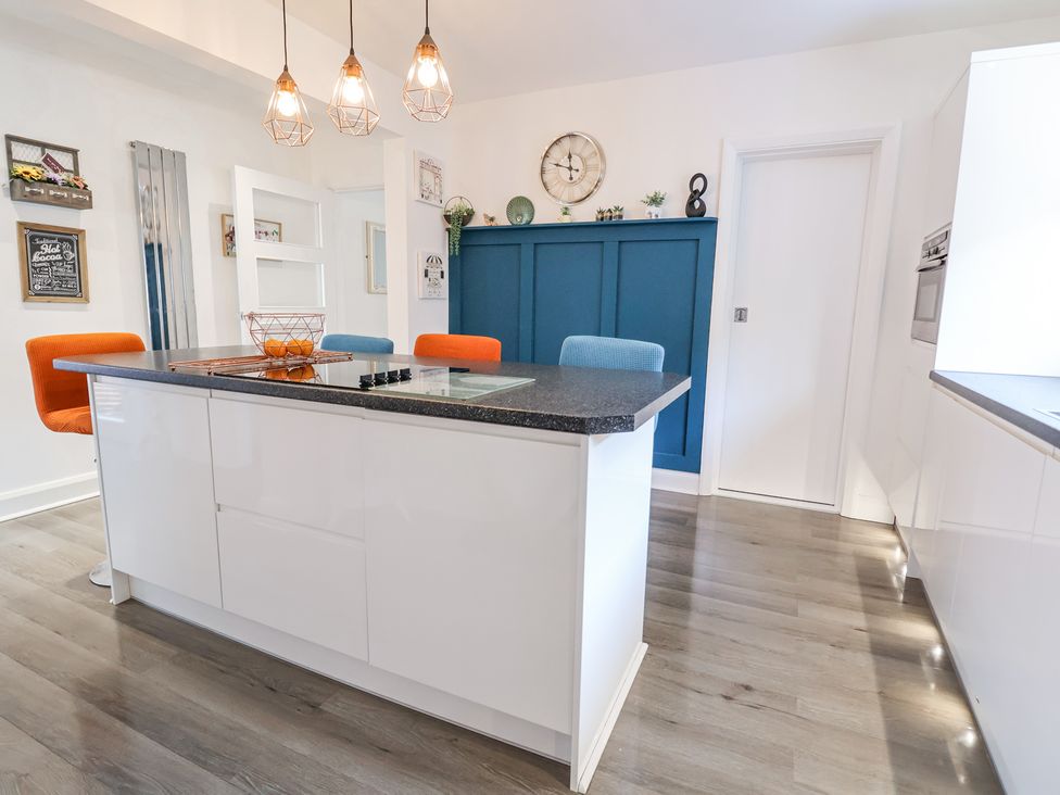 A kitchen with a white island and orange and blue chairs at 67 Pendre Avenue in Prestatyn
